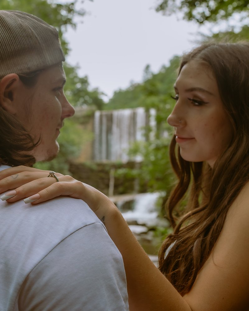Newly engaged couple looking at each other beside an Arkansas waterfall