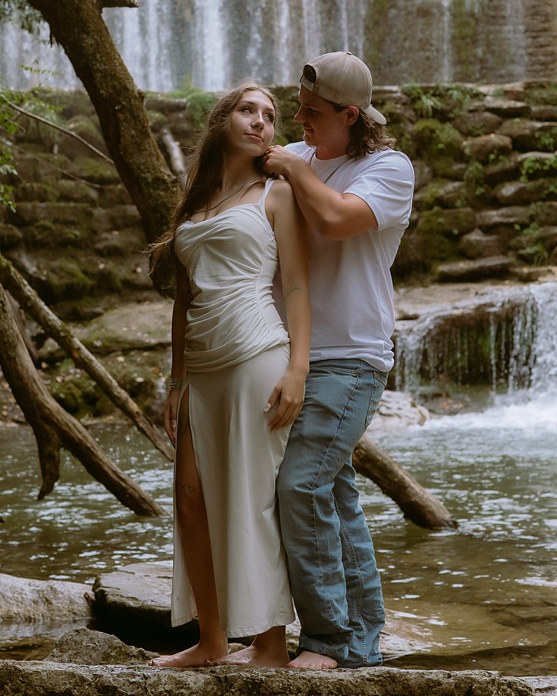 Newly engaged couple standing barefoot at the water edge below Mirror Lake Falls in Arkansas