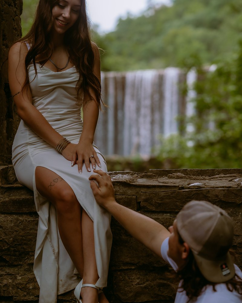 Engaged couple holding hands on the stone ledge below Mirror Lake Falls in Arkansas
