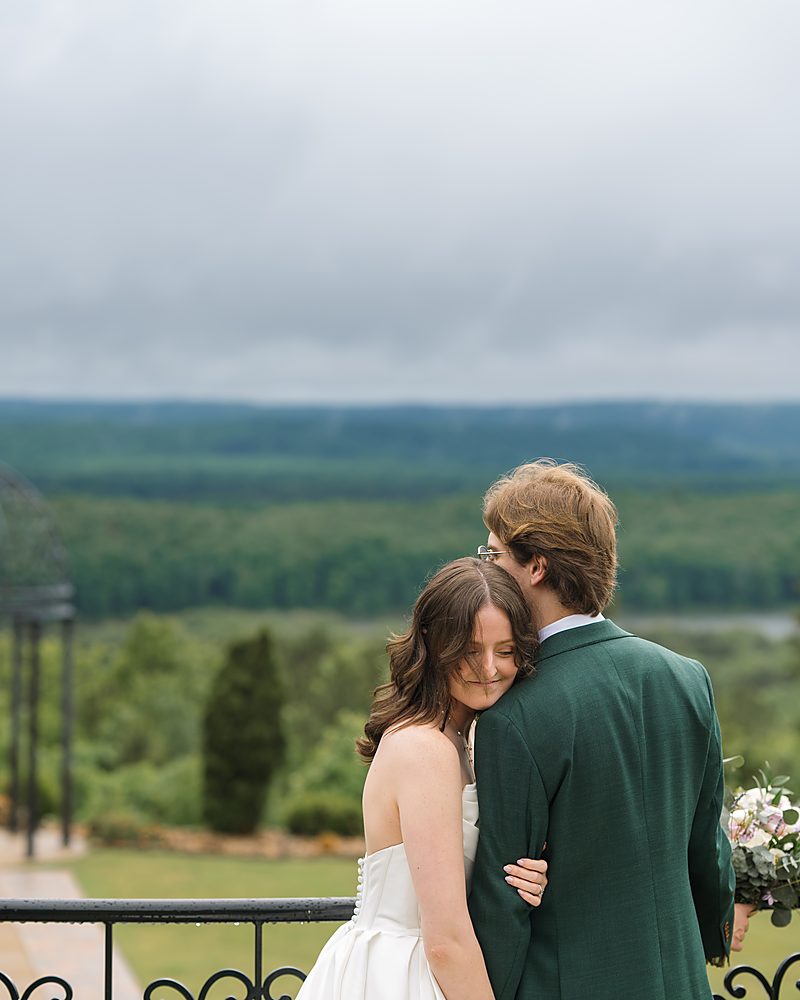 Newlyweds embracing above the tree-covered hills at a Central Arkansas venue