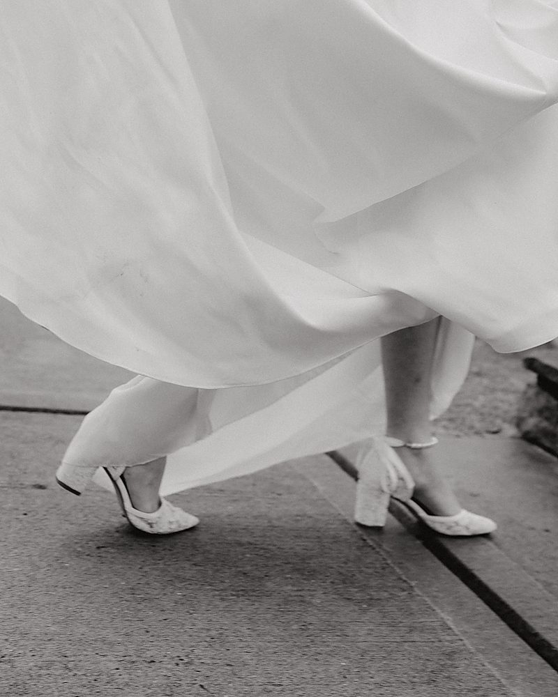 Black and white detail of a bride twirling her gown over her boots